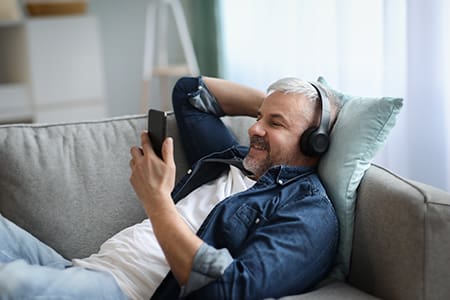 Joyful grey-haired man in headphones listening to music on smartphone