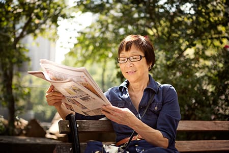Woman reading newspaper while sitting on bench at park
