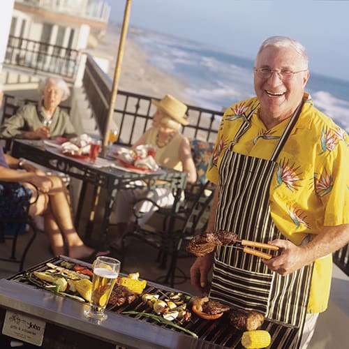 Smiling man grilling steaks and vegetables outdoors at Carlsbad by the Sea