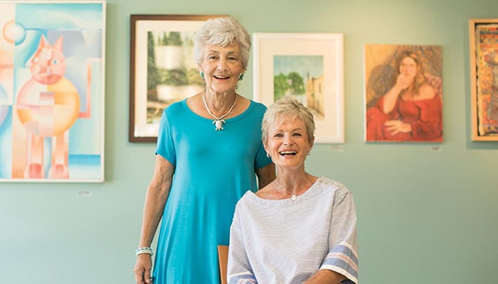 Portrait of two women smiling in front of a wall of artwork at Carlsbad by the Sea