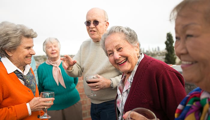 A group of older adults smile together while standing on a rooftop patio with views of LA in the background.