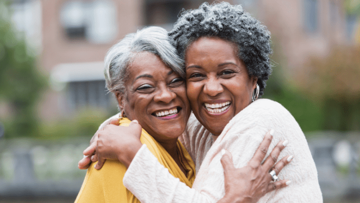 Two older women smile while giving each other a hug.