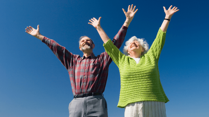 Two older adults raising their hands and looking happy.