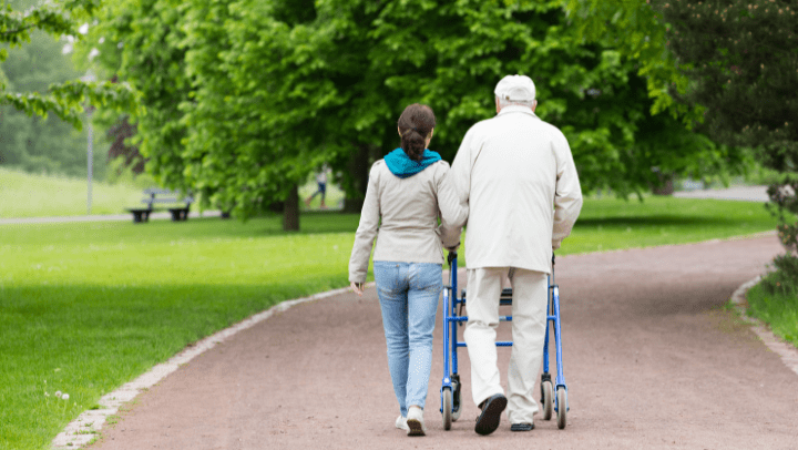 A caregiver walking with a senior outside in a park.