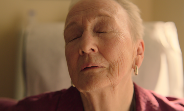 An older woman looks upwards with her eyes closed.