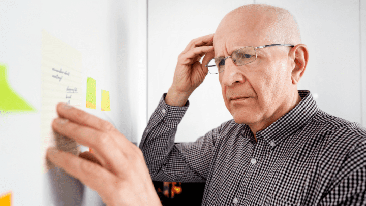 An older man contemplates a board with notes and post-its.