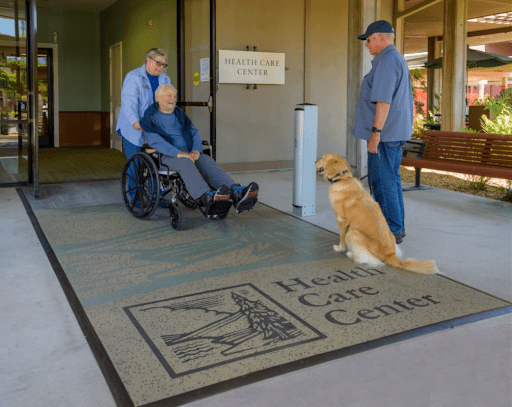 Caretaker bringing man in a wheelchair to meet a golden retriever brought by a resident.