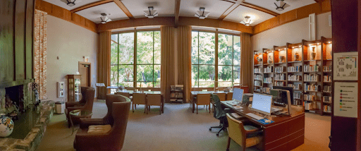 Panoramic view of a library with a fireplace on the left side and computers on the right. 