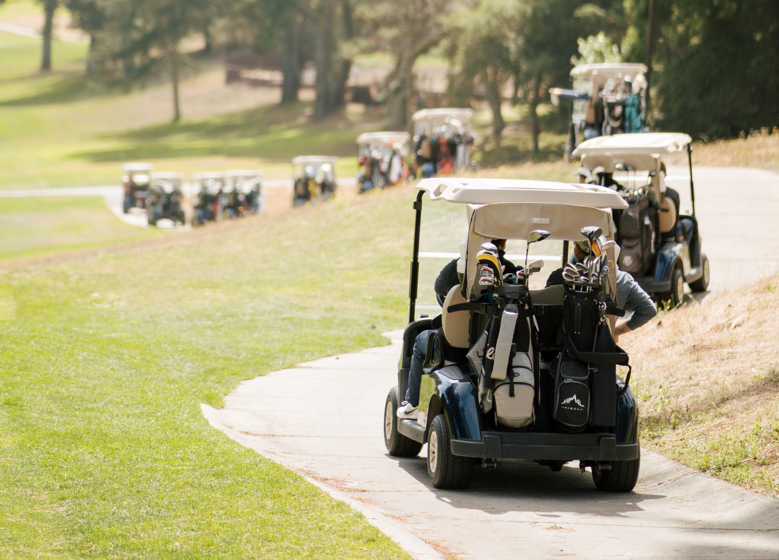 A line of golf carts drive off into the distance on a path wrapping around a golf course.