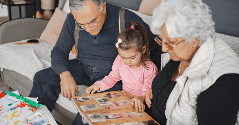 a grandparent couple looking at photos in their family album with their granddaughter