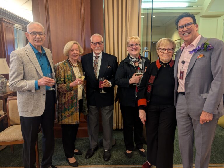 A group of people, some of whom are holding wine glasses, pose together.