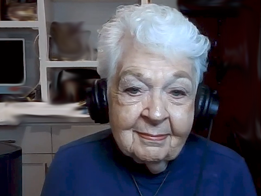 An older woman wearing headphones smiles.