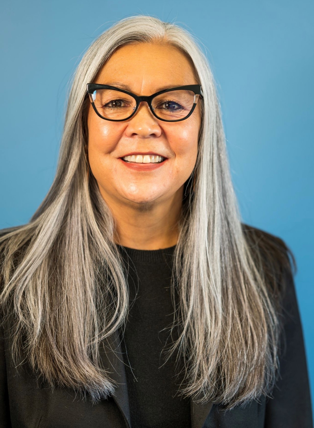 A headshot of a person with long gray hair and glasses.