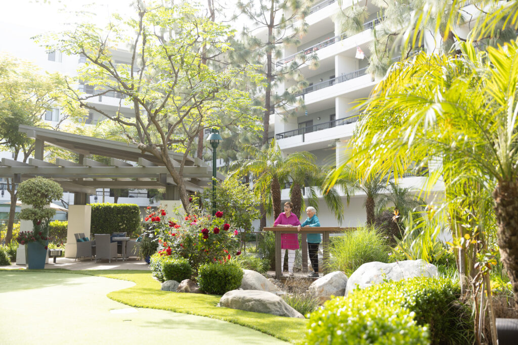 Two women stand in a garden outside white apartment building.
