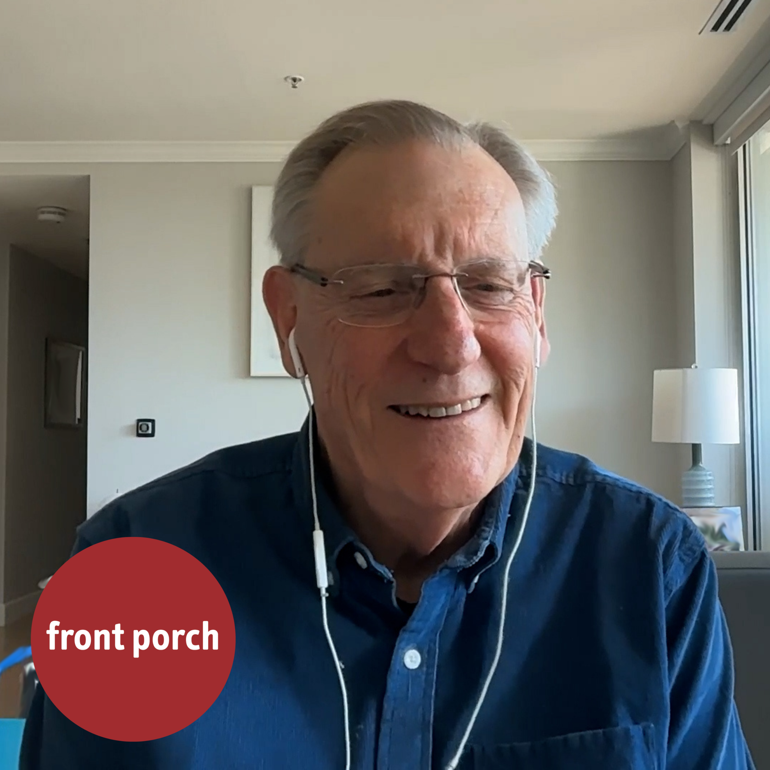 A man wearing glasses, a blue shirt and wired earbuds smiles.
