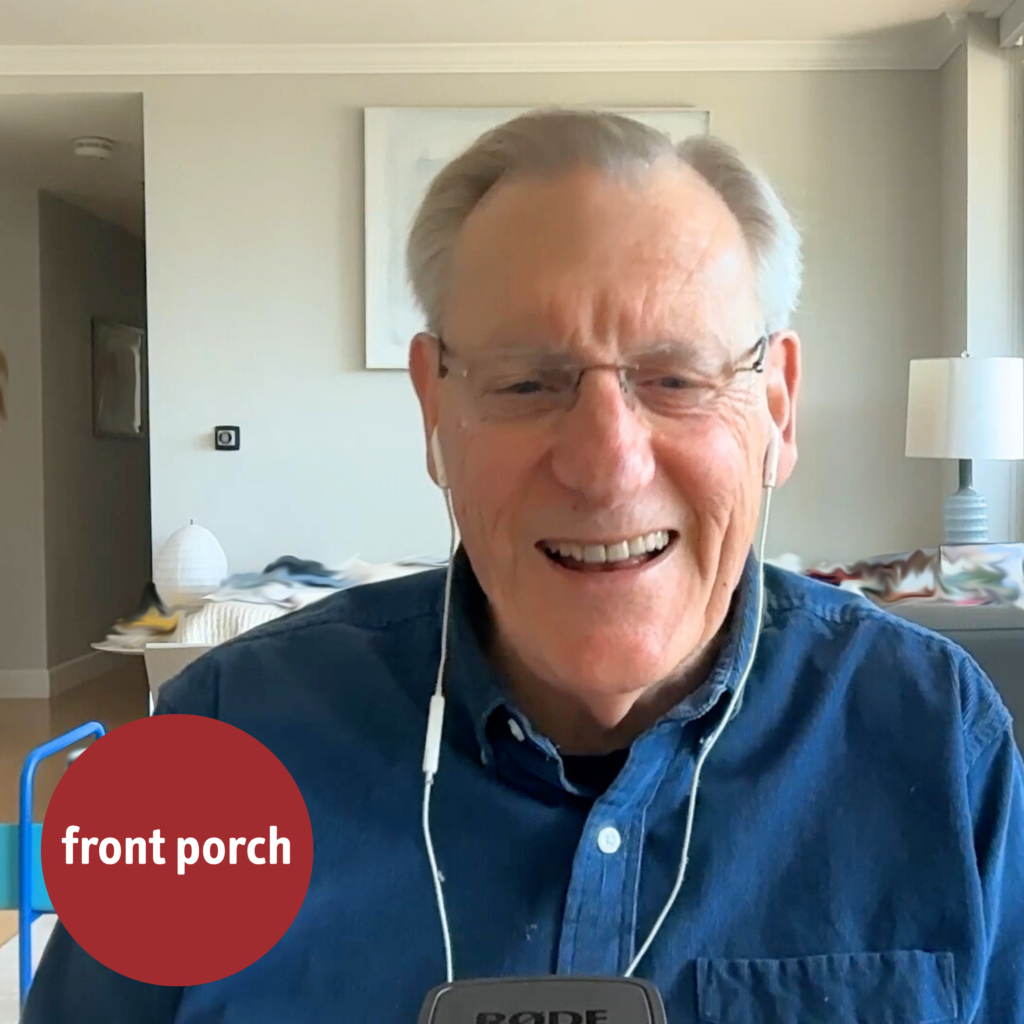 An older man wearing a blue button up shirt and wired earbuds smiles. The Front Porch ball logo is in the bottom left corner.