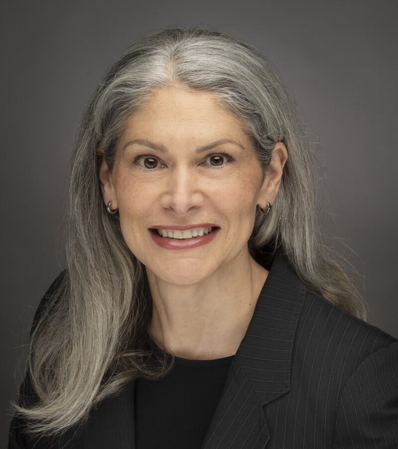 A Person With Long Hair, Wearing A Black Shirt And Blazer.