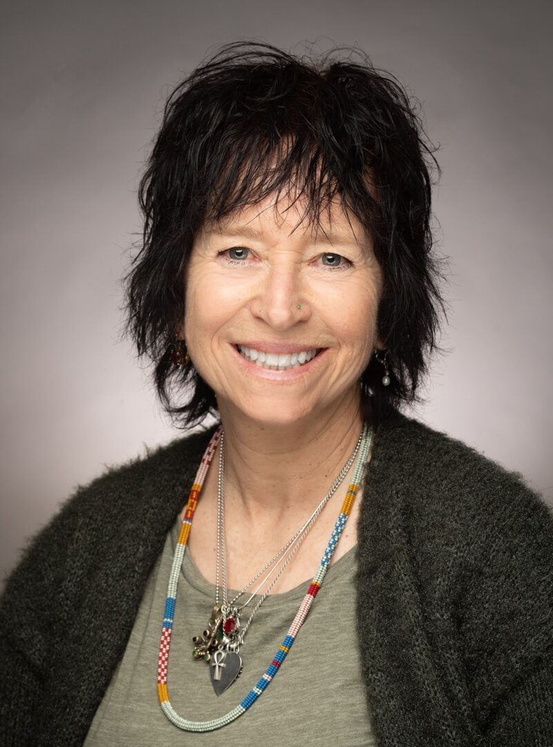 A Person Wearing A Green Shirt, Black Cardigan And A Collection Of Necklaces.