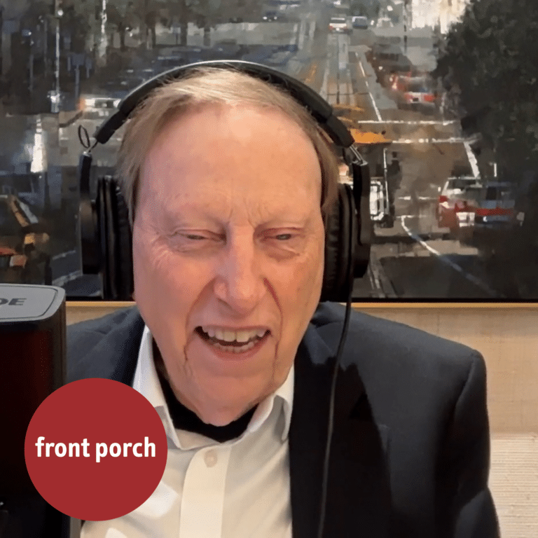 An Older Man Smiles While Wearing Headphones And Sitting Behind A Microphone.