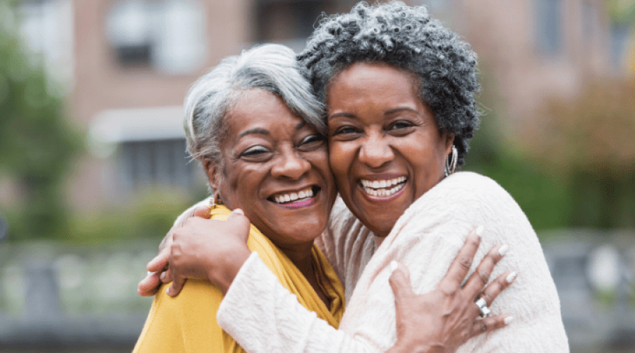 Two older women smile while giving each other a hug.