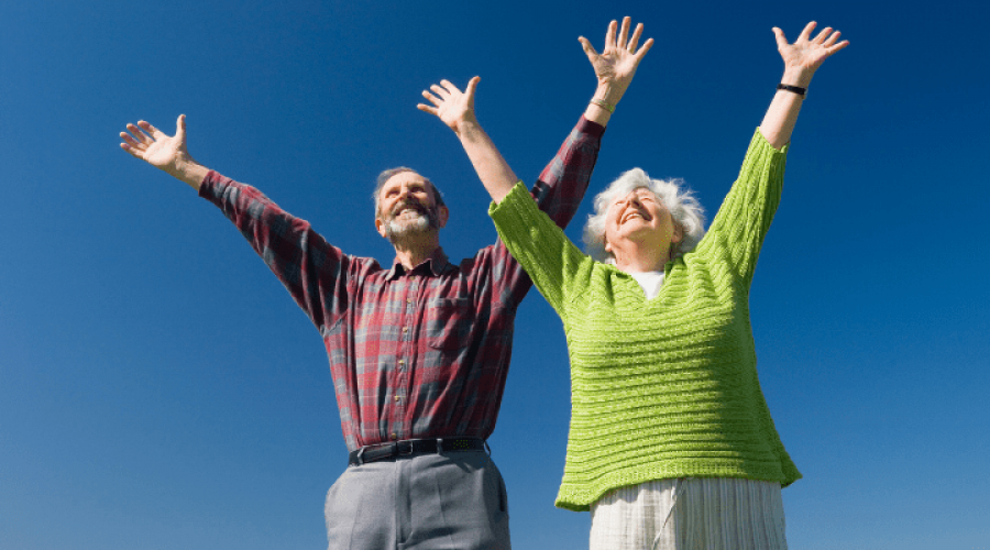 Two older adults raising their hands and looking happy.