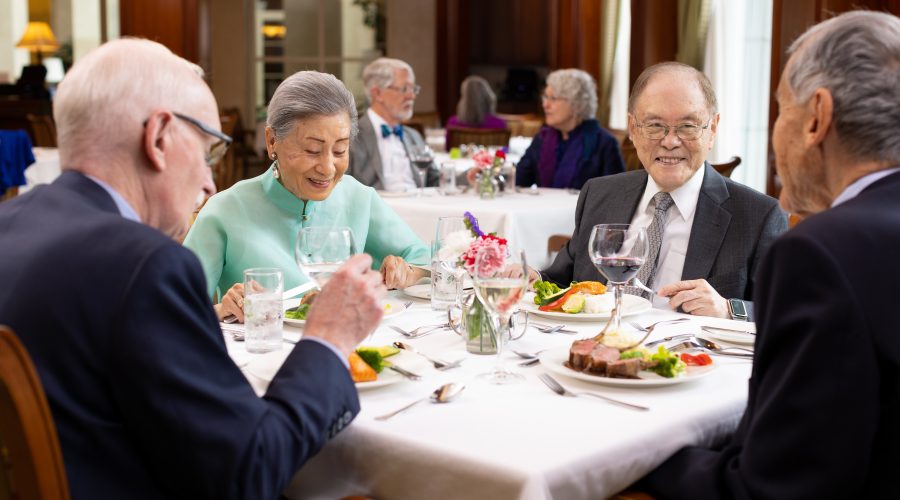 a group of seniors smiling at each other while enjoying their dinner