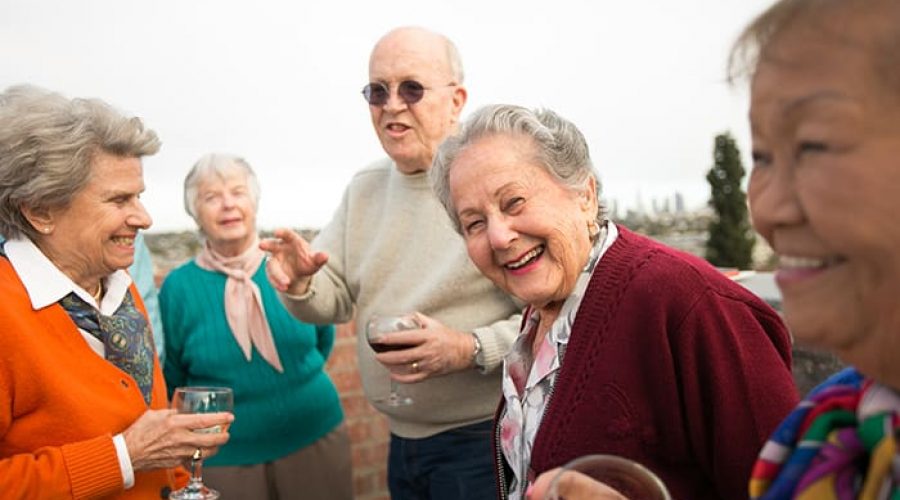 A group of older adults smile together while standing on a rooftop patio with views of LA in the background.