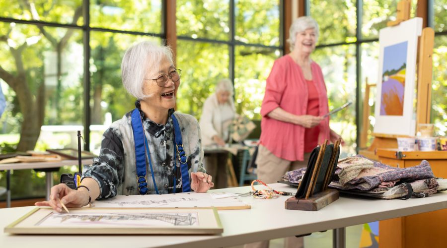 A group of people working on art projects in an art studio with big windows that showcase green trees and natural light