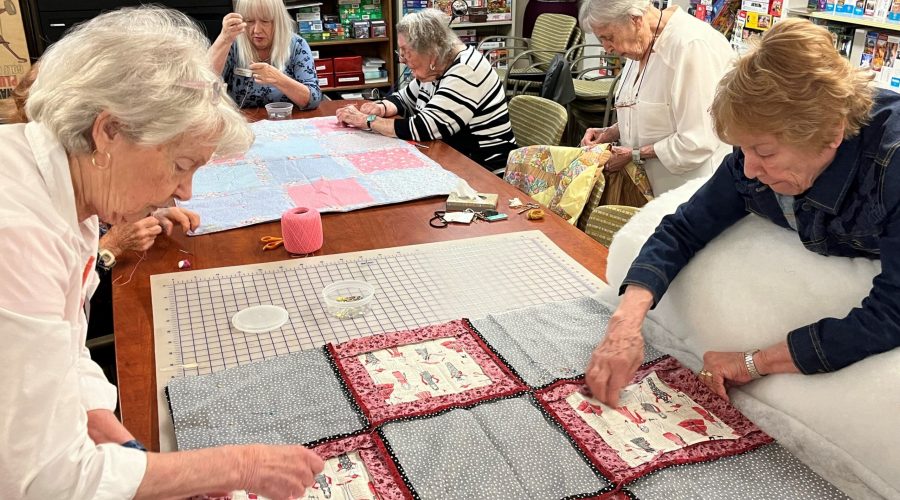 Women gather around a table sewing on small quilts