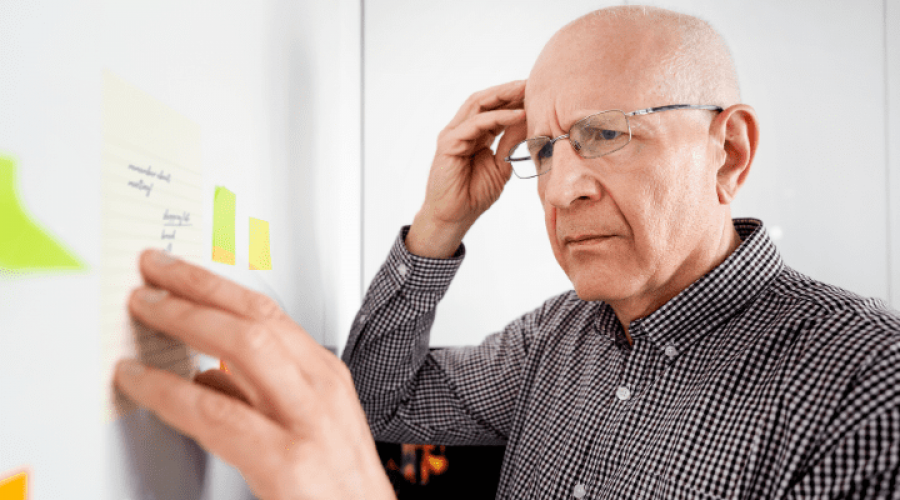 An older man contemplates a board with notes and post-its.