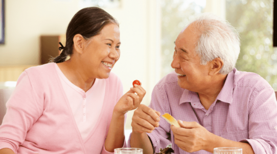 Two older adults smile together while holding fruit.