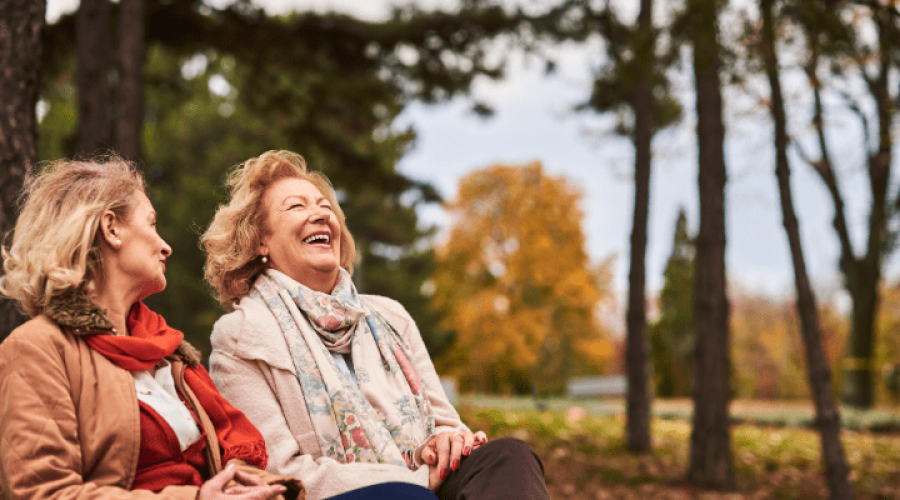 Two women laugh outside in Autumn.