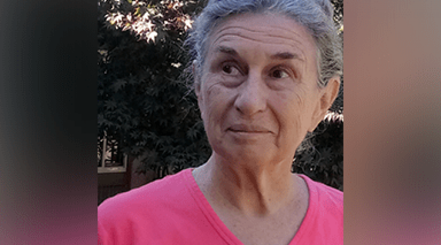 A woman wearing a pink shirt smiles while looking off screen.